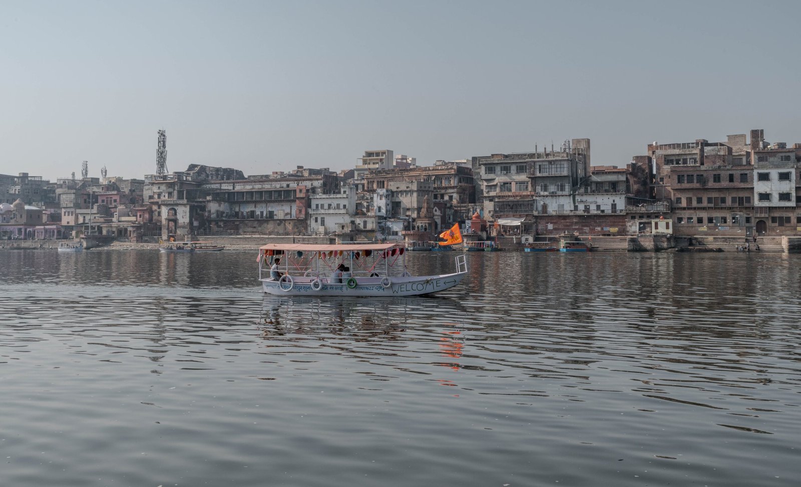 Boat cruising on the Yamuna River with Mathura cityscape in Uttar Pradesh, India.