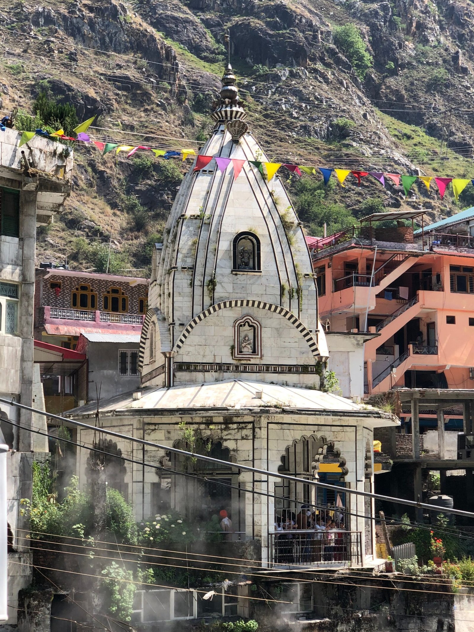 A picturesque Hindu temple surrounded by colorful flags in a mountainous region.