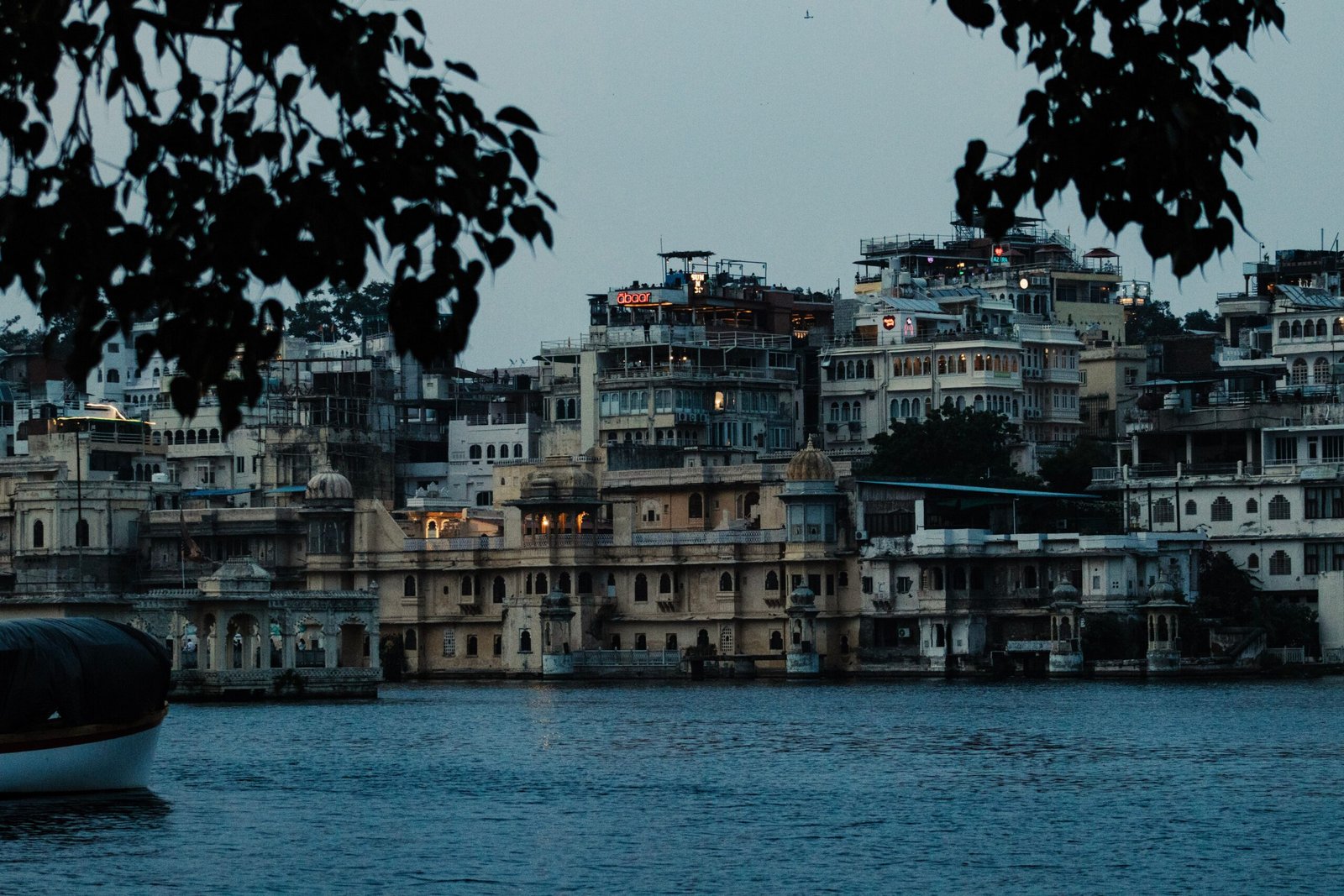 Scenic view of Udaipur's City Palace and surrounding architecture seen from Lake Pichola at dusk.